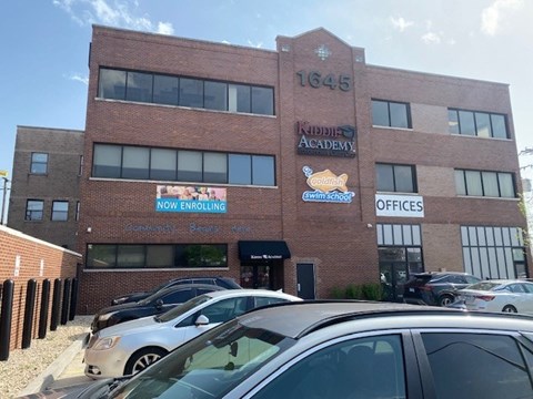 A brick building with a sign that says "Now Enrolling" in front of it.