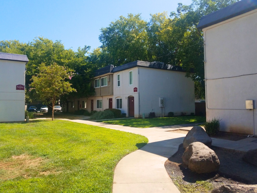 A white building with a red door is surrounded by trees and a grassy area.