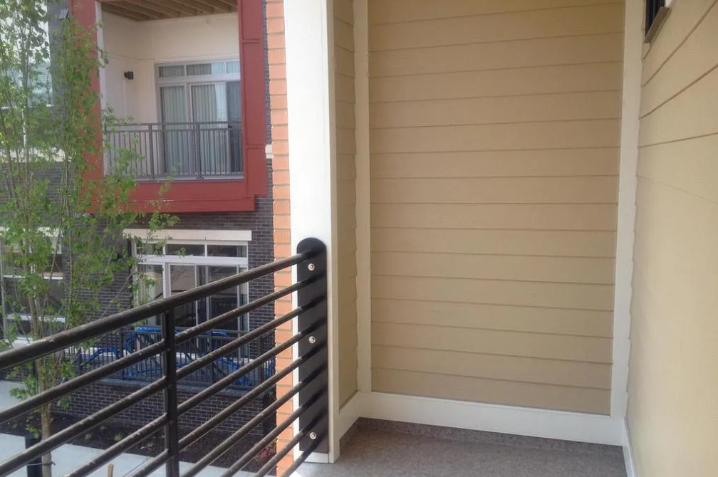 A balcony with a black railing and a red building in the background.