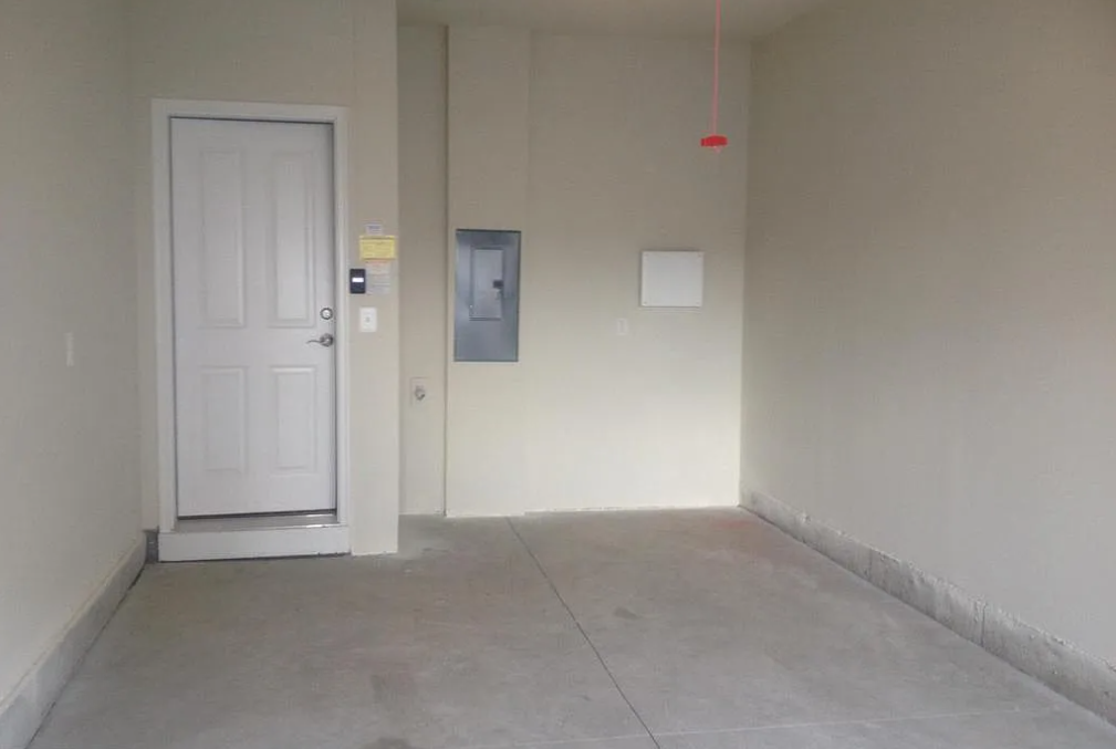 A white door is on the left side of a room with a grey floor.