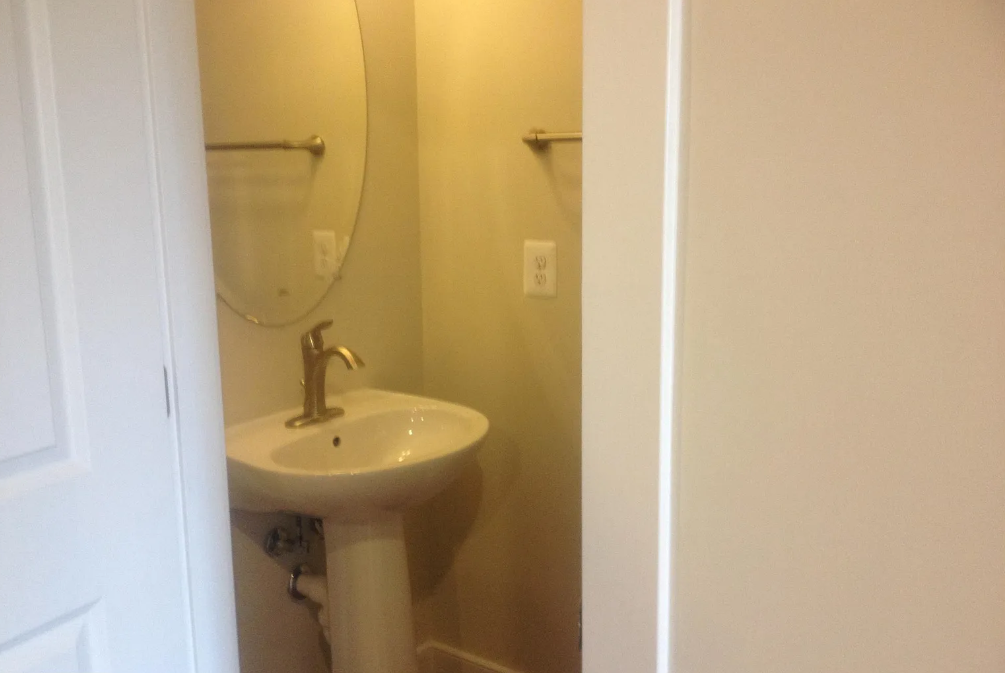 A white pedestal sink with a silver faucet and a round mirror above it.