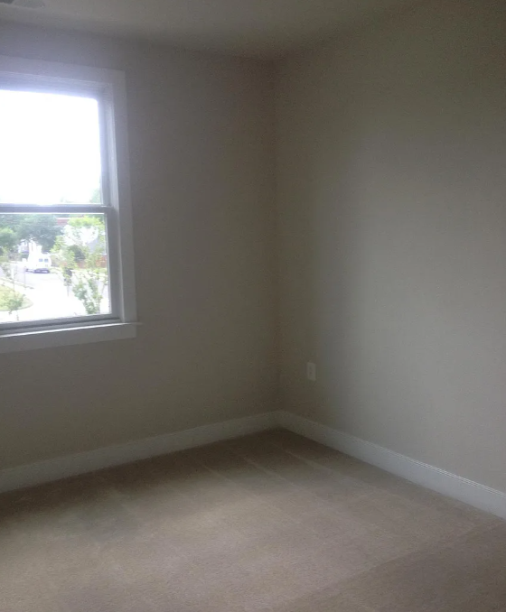 A room with a window and car parked outside.