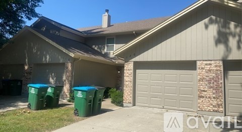 A house with a garage and three green bins in front.