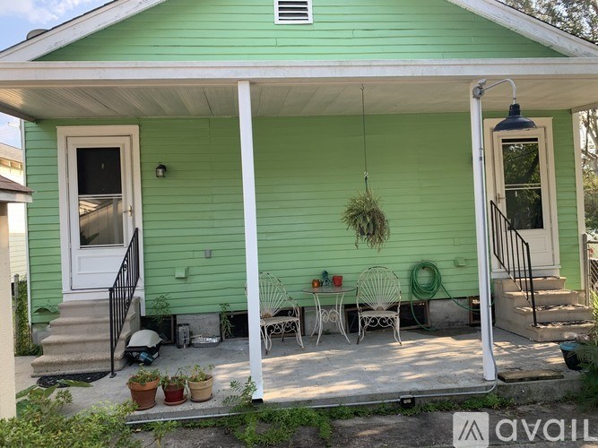 A green house with a porch and a hanging plant.