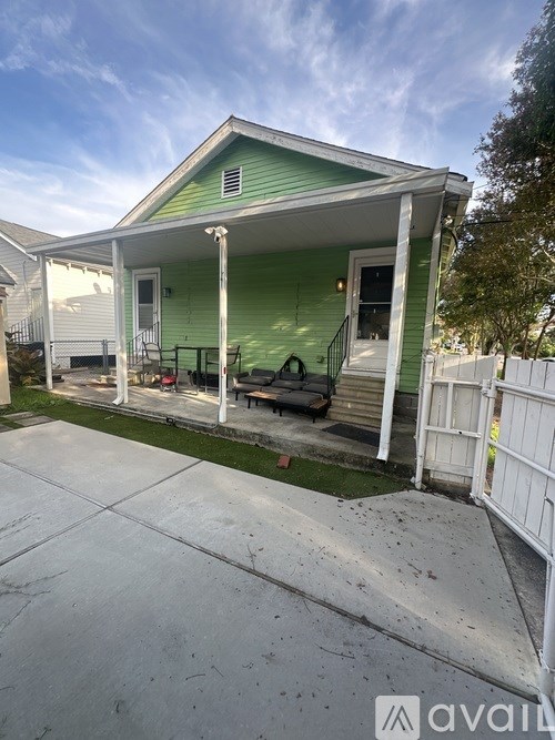 A green house with a white porch and a white fence.