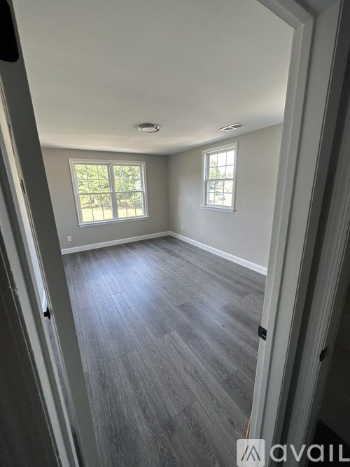 A room with grey flooring and two windows.