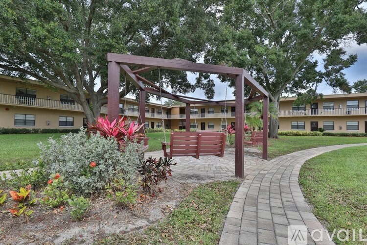 A red wooden pergola is in the middle of a garden with a walkway leading to a building.