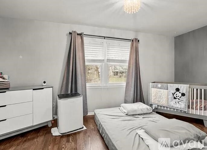 A white bedroom with a bed, a dresser, a window with curtains, and a Disney-themed crib.