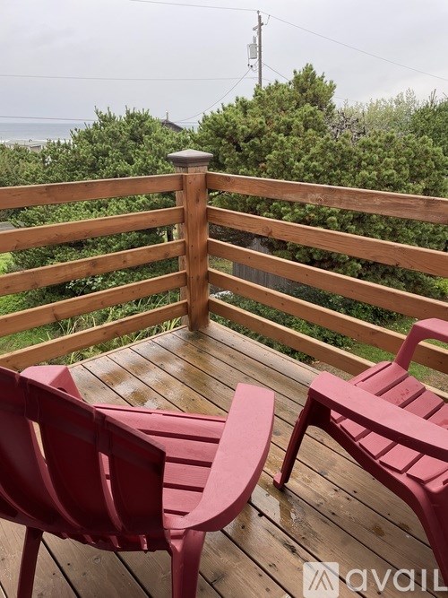 Two red chairs on a wooden deck overlooking the ocean.