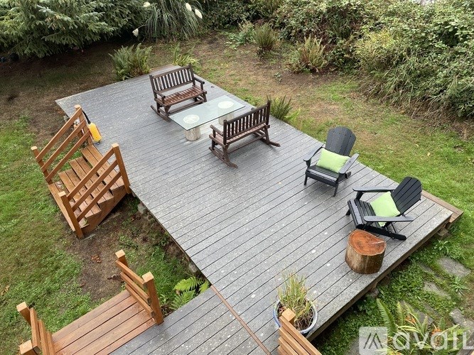 A wooden deck with chairs and a table surrounded by greenery.