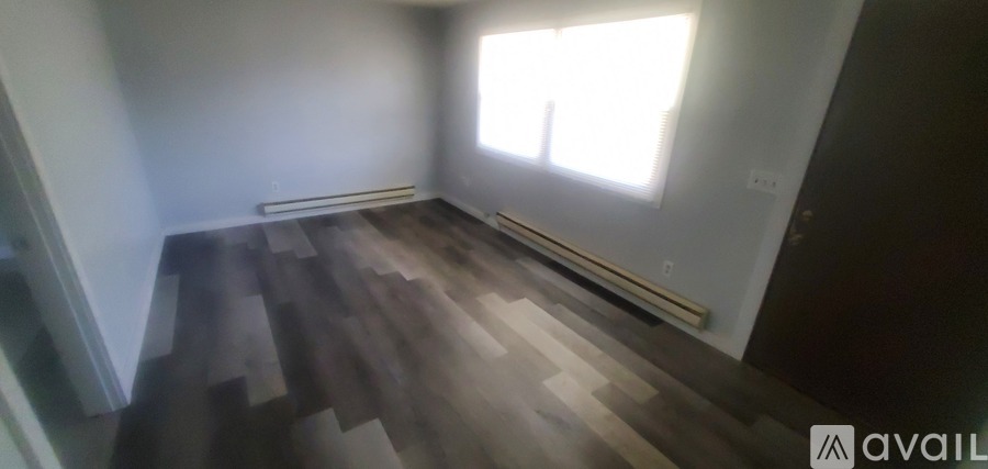 A room with wooden flooring and a window letting in sunlight.