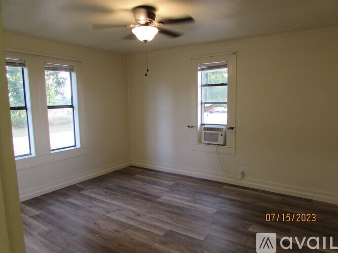 A room with a ceiling fan and two windows.