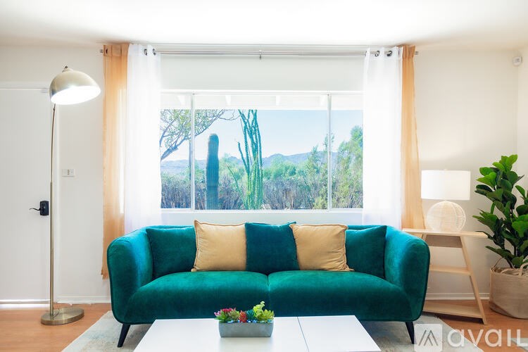 A green couch with two pillows sits in front of a window with a view of trees and mountains.