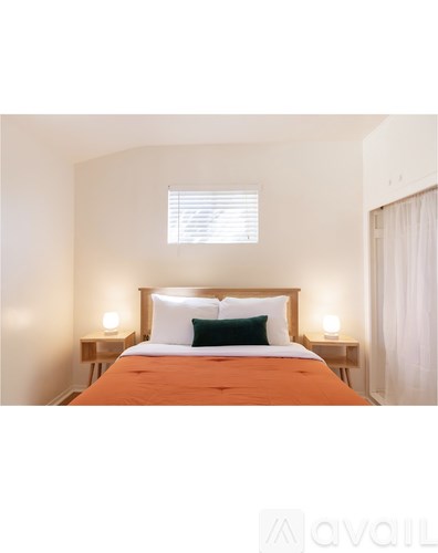 A bedroom with a bed, two lamps, and a window.