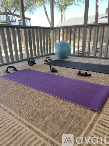 A purple yoga mat is on a wooden floor with a blue ball and two black kettlebells.