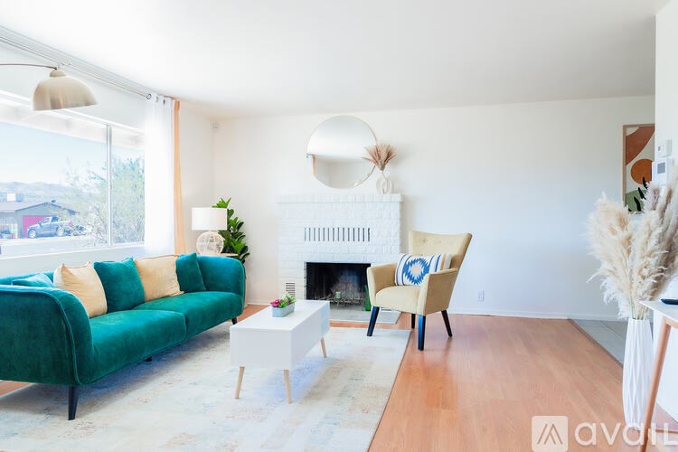 A living room with a green couch, a white fireplace, and a large window.