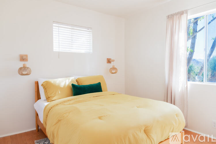 A bedroom with a bed covered in a yellow comforter and two green throw pillows.