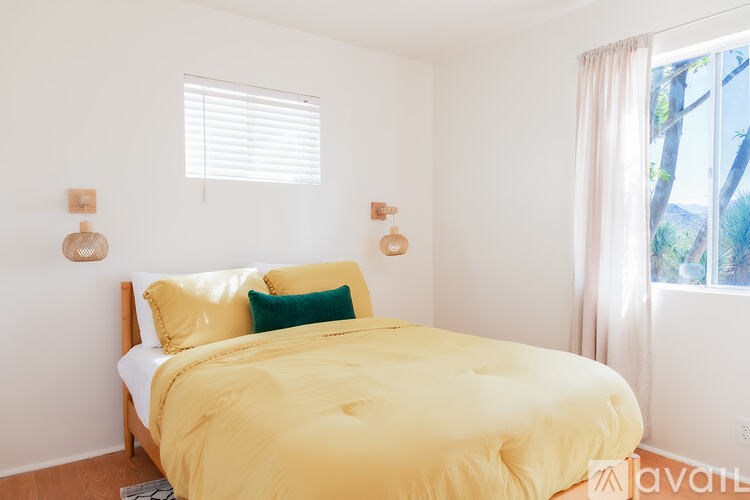 A bedroom with a bed covered in a yellow comforter and two green throw pillows.
