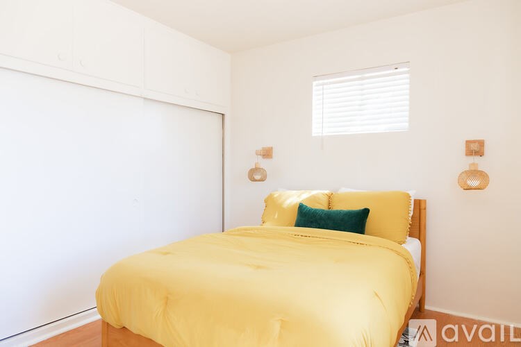 A bed with a yellow cover and a green pillow is in a room with white walls.
