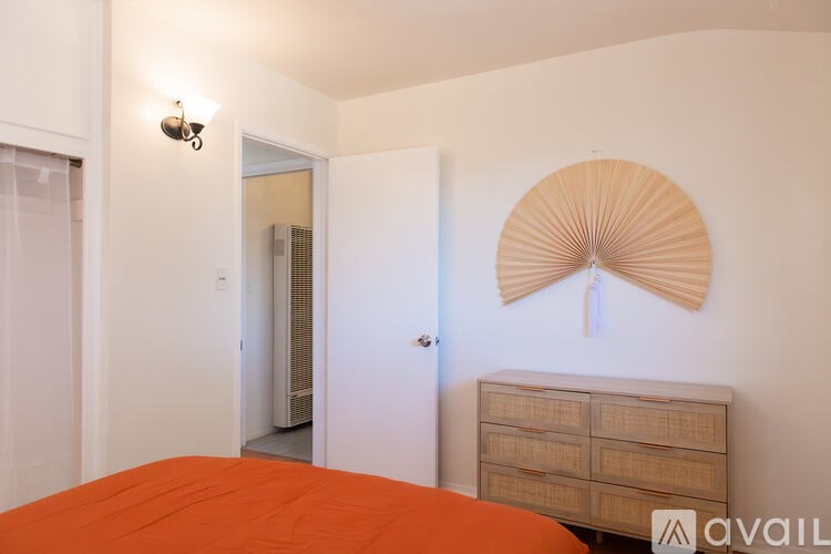 A bedroom with a bed, dresser, and a wall fan.