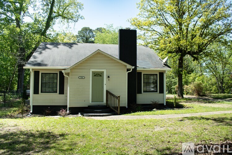 A small white house with a black chimney is surrounded by greenery.
