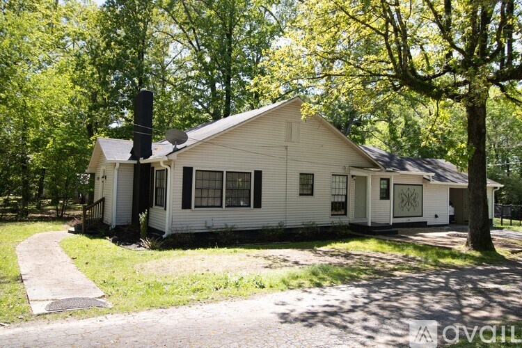 A white house with a satellite dish on the roof is surrounded by trees.