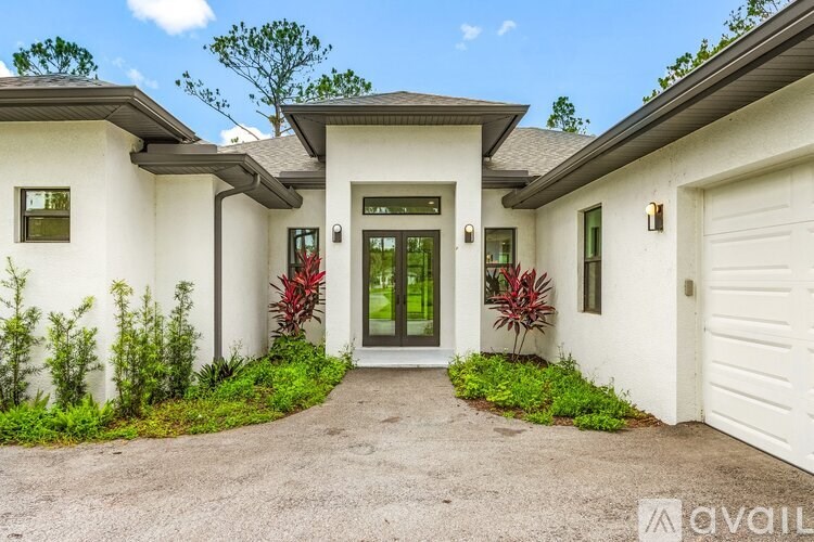 A white house with a grey roof and a green plant in front.