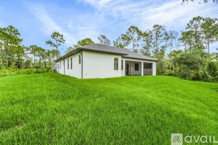 A white house with a grey roof is surrounded by green grass and trees.