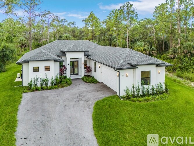 A white house with a grey roof is surrounded by greenery.