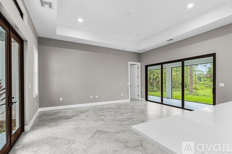 A spacious room with a marble floor and sliding glass doors leading to a green outdoor area.