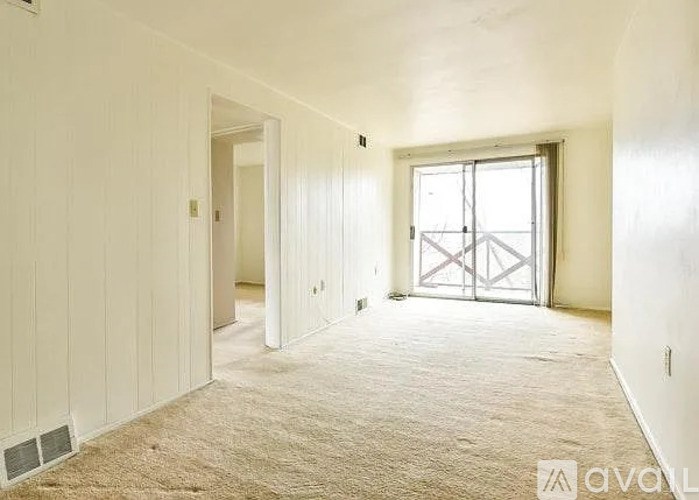 A room with a carpeted floor and a window with a metal gate.