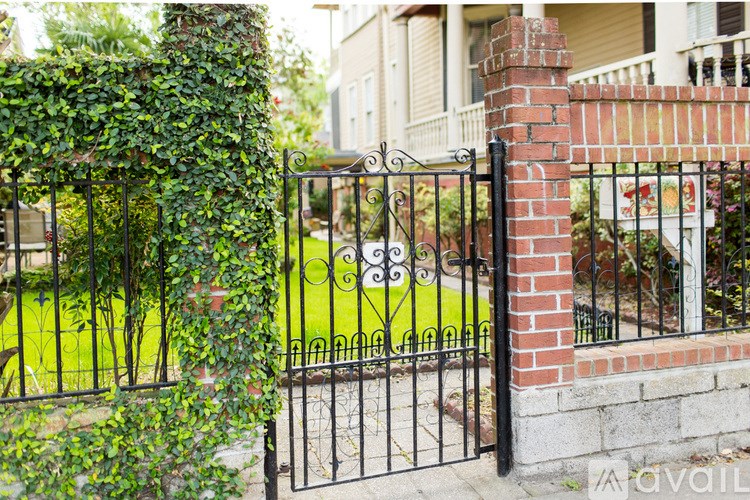 A black iron gate with a brick pillar and a sign on it.