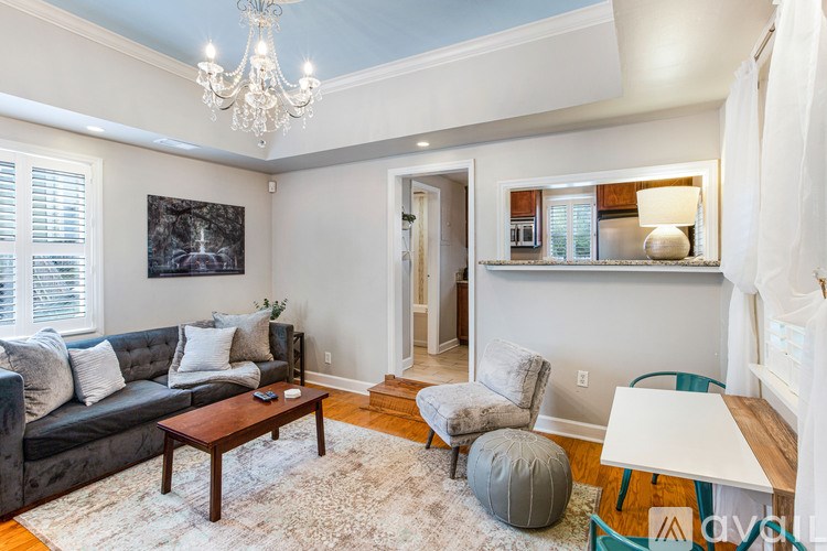 A living room with a grey couch, a coffee table, a chair, a bean bag, a rug and a chandelier.