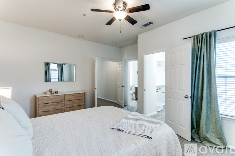 A bedroom with a white bed, a ceiling fan, and a dresser with a mirror.