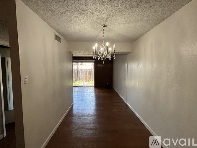 A long hallway with a chandelier and a door at the end.
