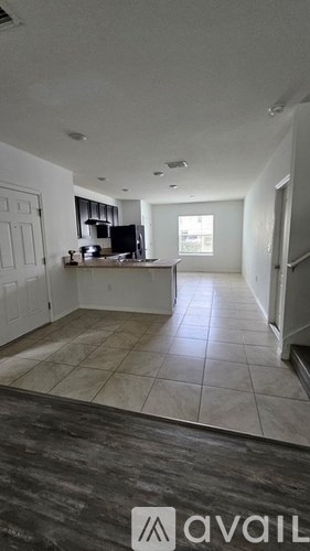 A spacious living room with a kitchen area in the background.