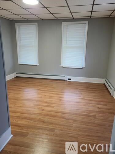 A room with wooden flooring and two windows.