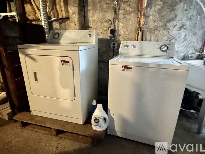 Two white ovens are on a wooden pallet in a room with a stone wall.