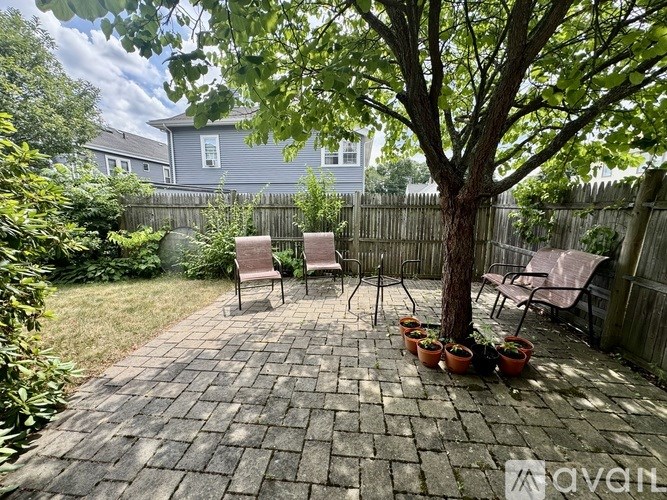 A backyard with a tree, chairs, and potted plants.