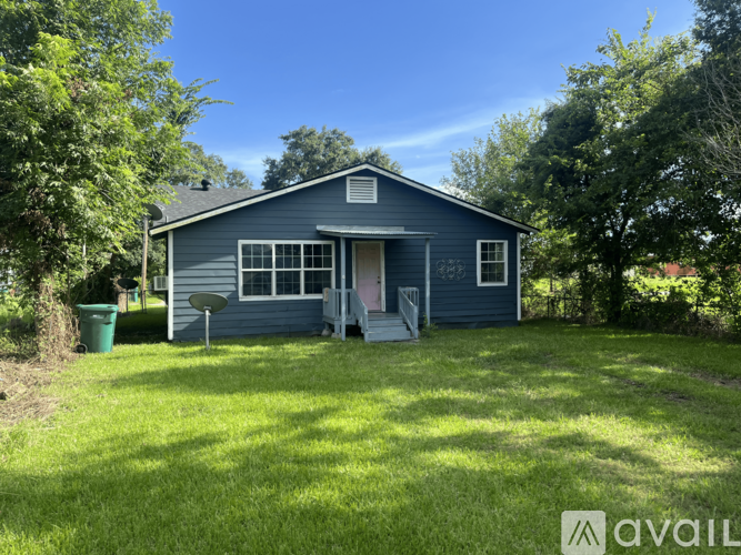 A blue house with a white door and windows is surrounded by green grass and trees.