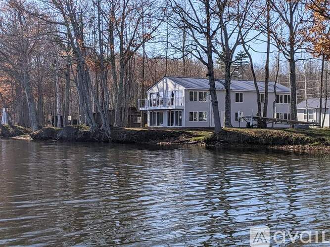 A house is situated on the water's edge with trees in the background.