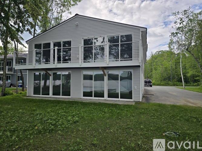 A house with a grey roof and white walls is surrounded by greenery.