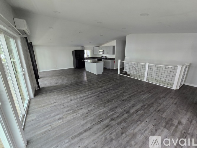 A spacious room with wooden flooring and a kitchen area in the background.