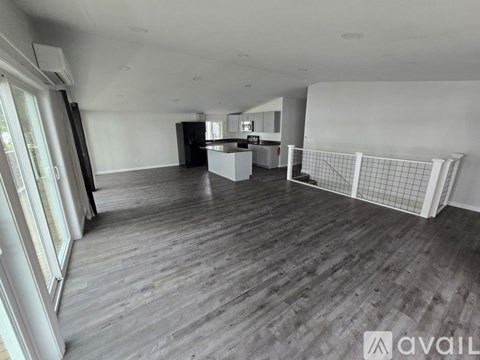 A spacious room with wooden flooring and a kitchen area in the background.