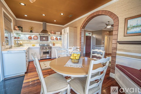 A kitchen with a table and chairs in the foreground and a refrigerator with a pot on top.