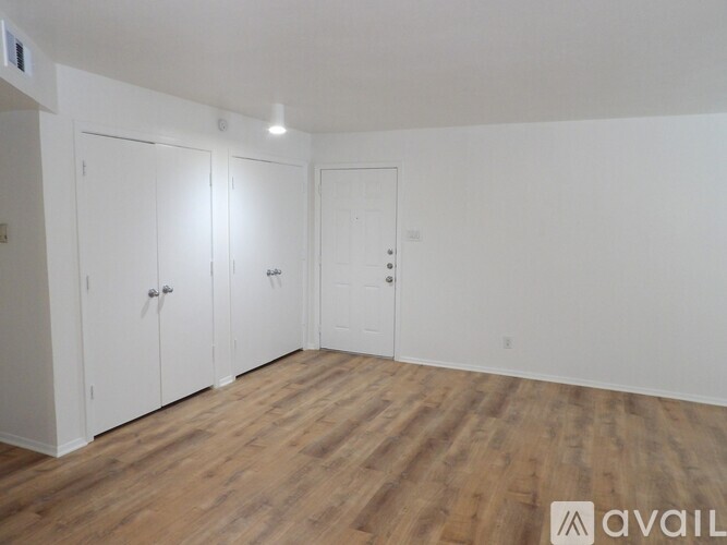 A room with white walls and wooden flooring, featuring three white doors.