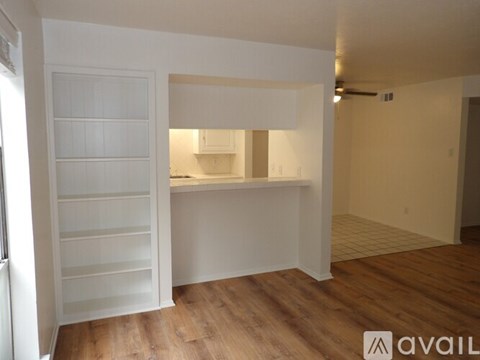 A room with a white door and a kitchen area in the background.