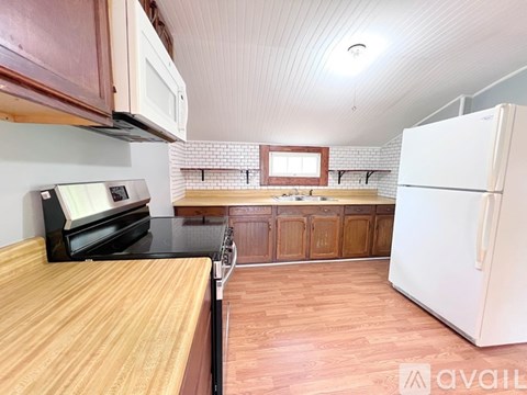A kitchen with a white fridge, wooden countertops, and a black stove top oven.
