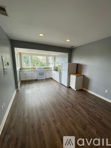 A room with wooden floors and a window overlooking a kitchen.