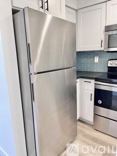A stainless steel refrigerator stands in a kitchen with white cabinets.
